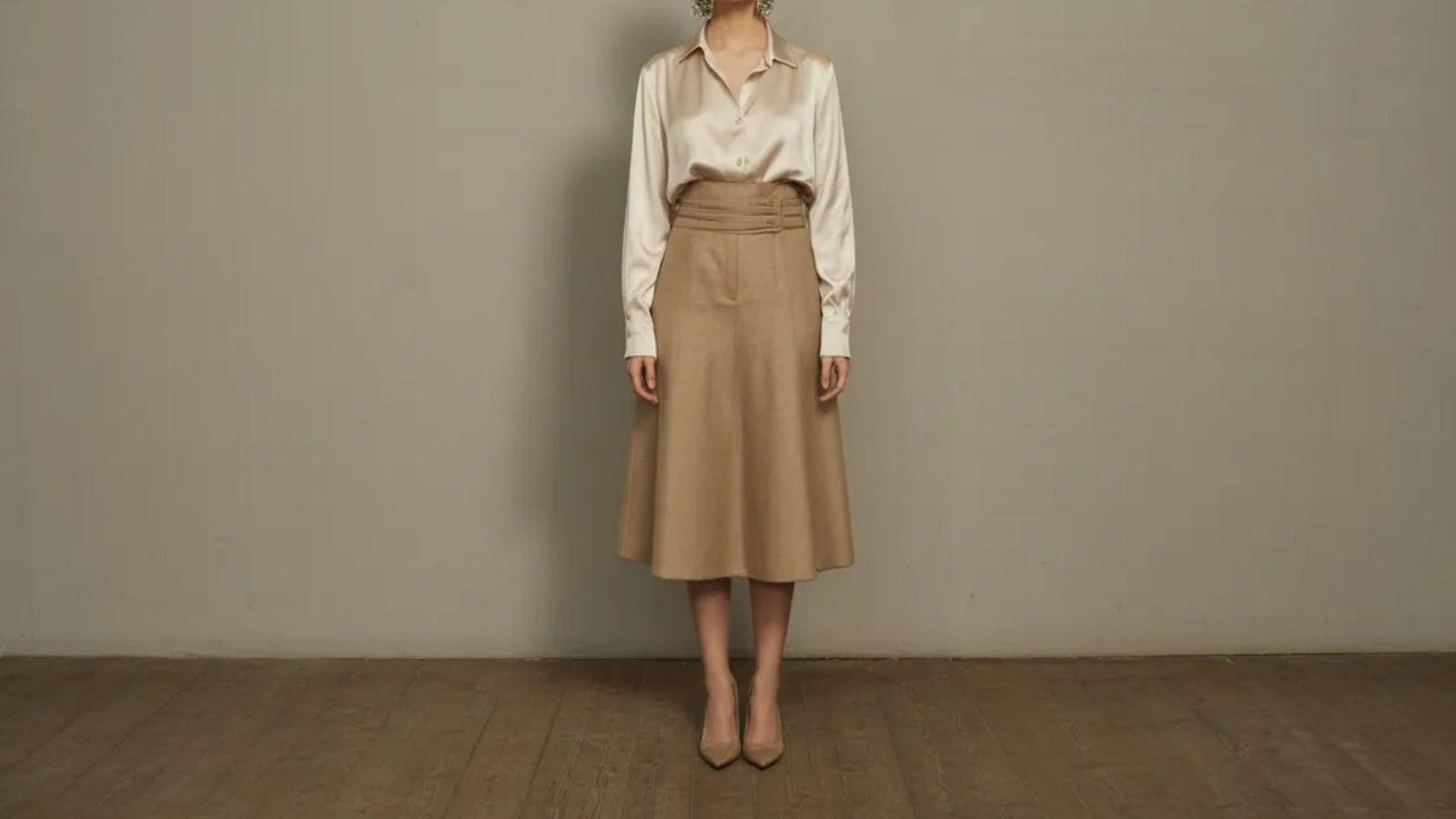  A woman wearing a white shirt and tan skirt stands confidently, showcasing a casual yet stylish outfit.