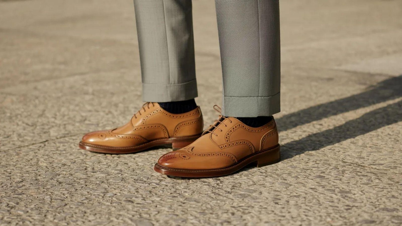 A man in a suit stands confidently, wearing brown shoes that complement his formal attire.
