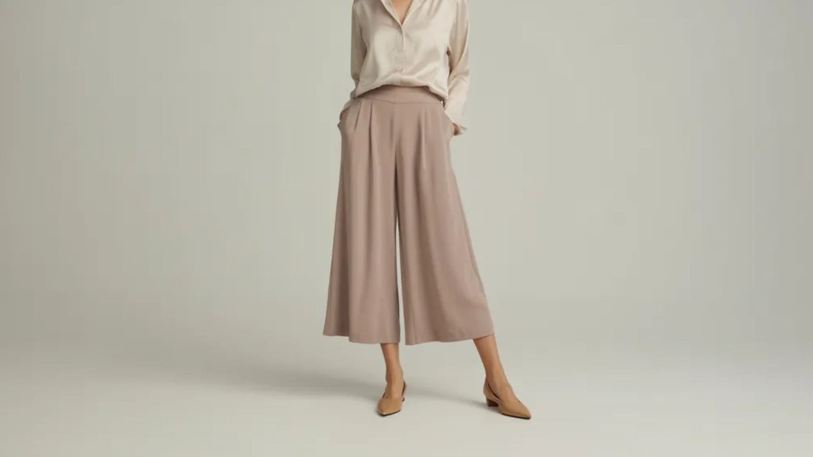  A model showcases a beige blouse paired with wide-leg trousers, highlighting a stylish and relaxed outfit.