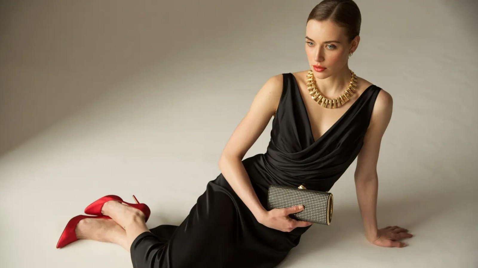 A woman wearing a black dress and red heels stands confidently, showcasing her elegant style.