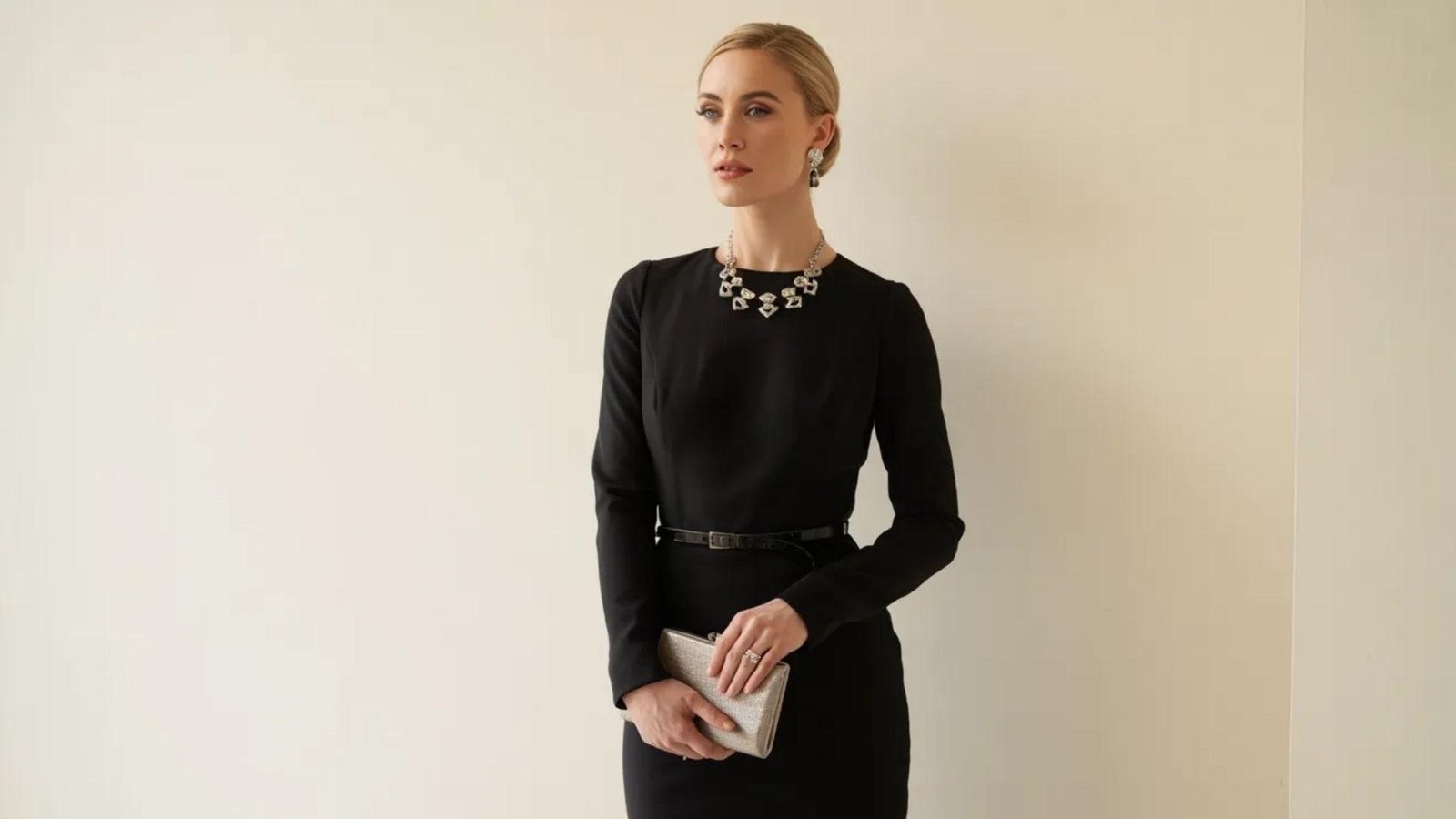 A woman wearing a black dress and a necklace, posing elegantly against a neutral background.