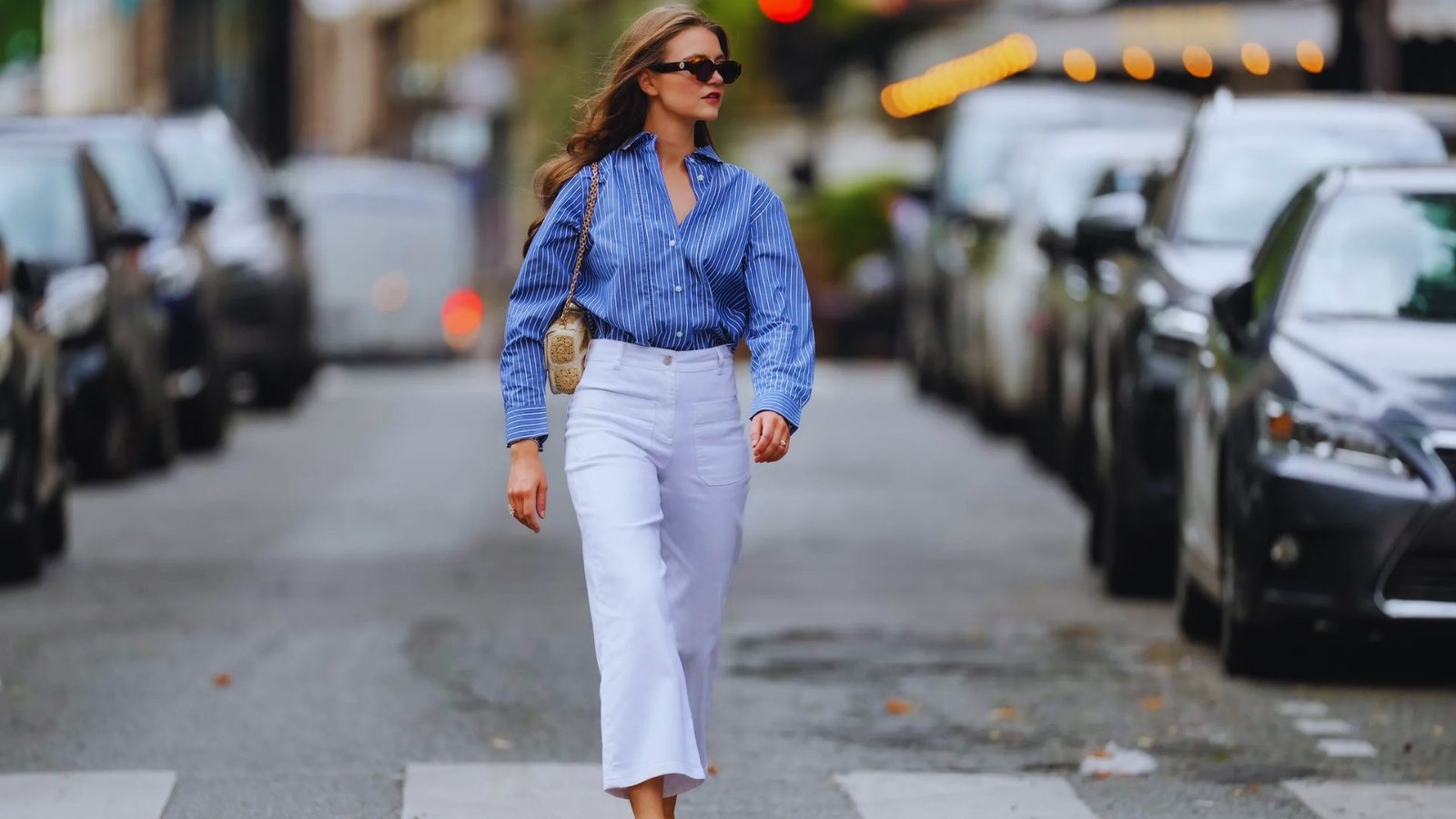 A woman wearing a blue shirt and white pants is crossing the street.