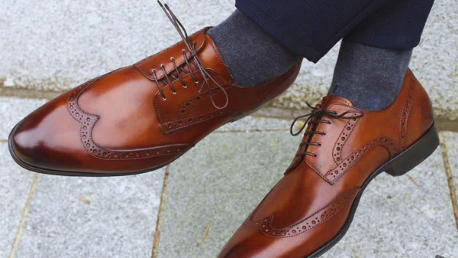 A close-up of a man's feet in brown shoes, showcasing the shoe design and texture against a neutral background