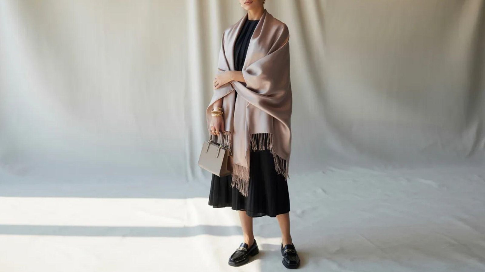 A woman in a pink shawl over a black dress, standing gracefully with a neutral expression.