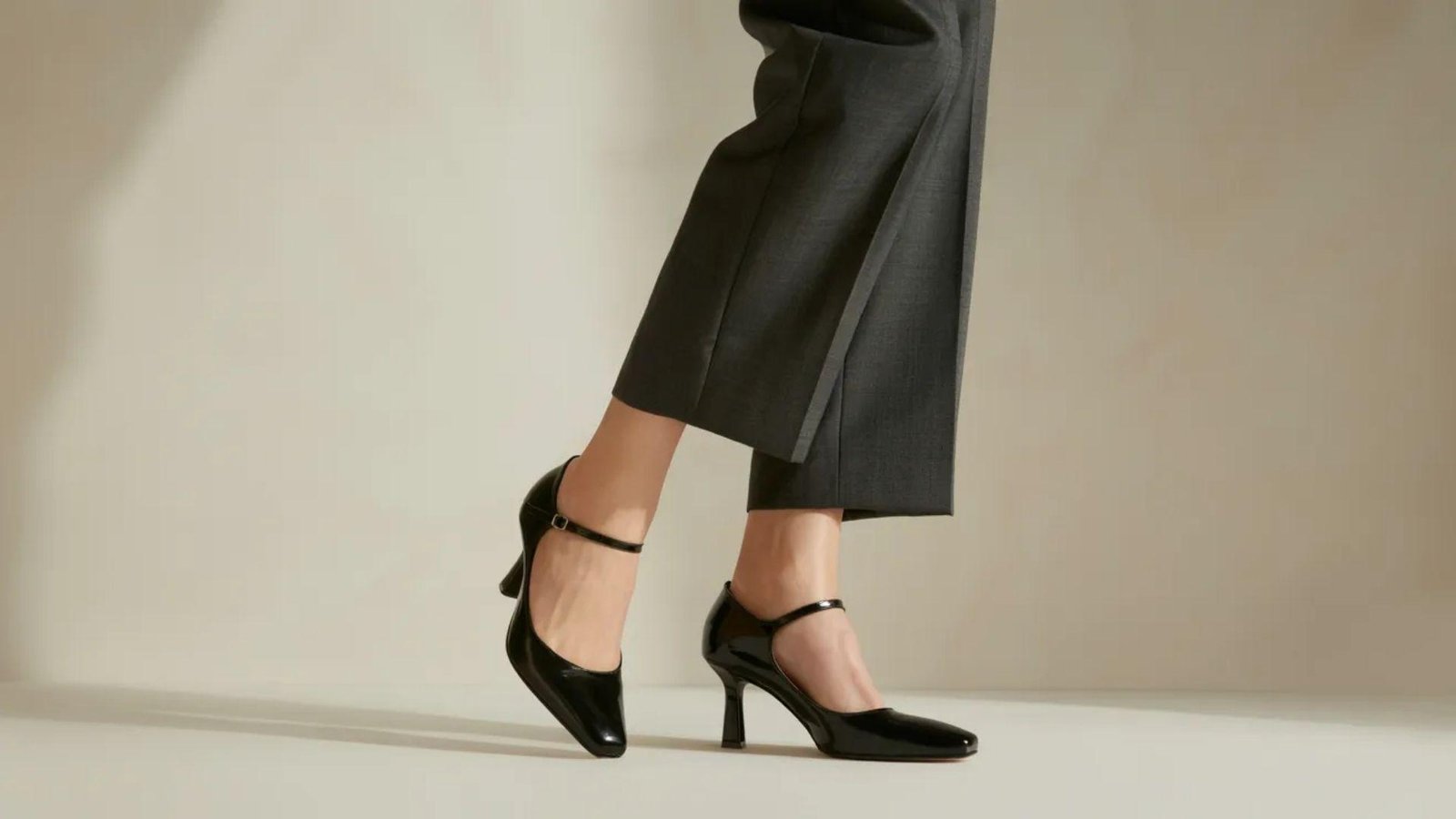 A woman in a grey suit and black pumps stands confidently, showcasing a professional and stylish appearance.