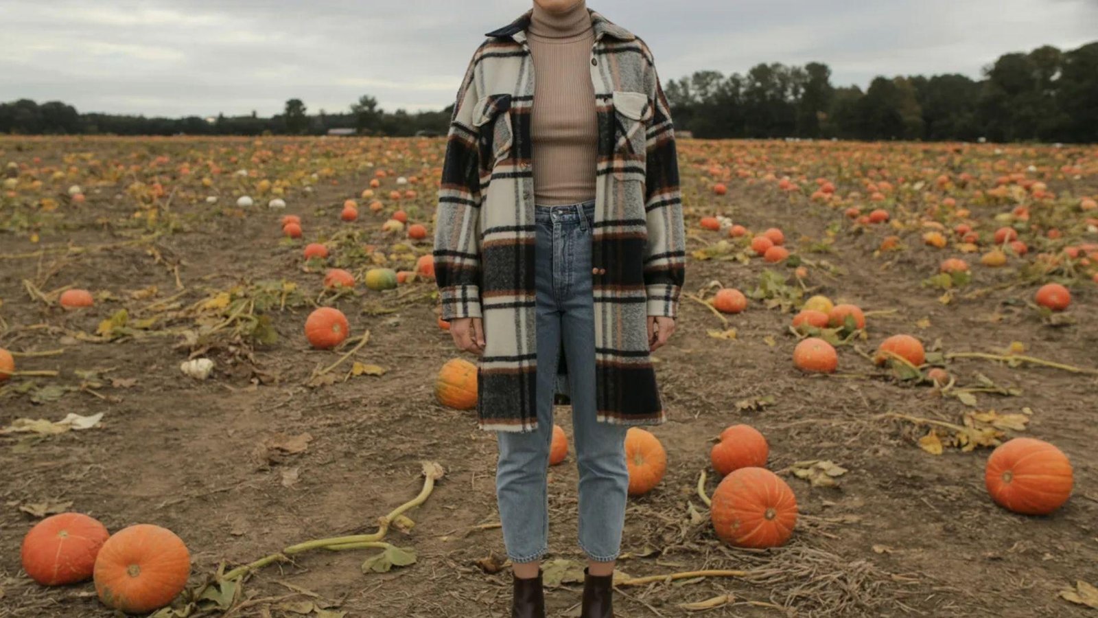  A woman stands among vibrant orange pumpkins in a sprawling pumpkin field under a clear blue sky.
