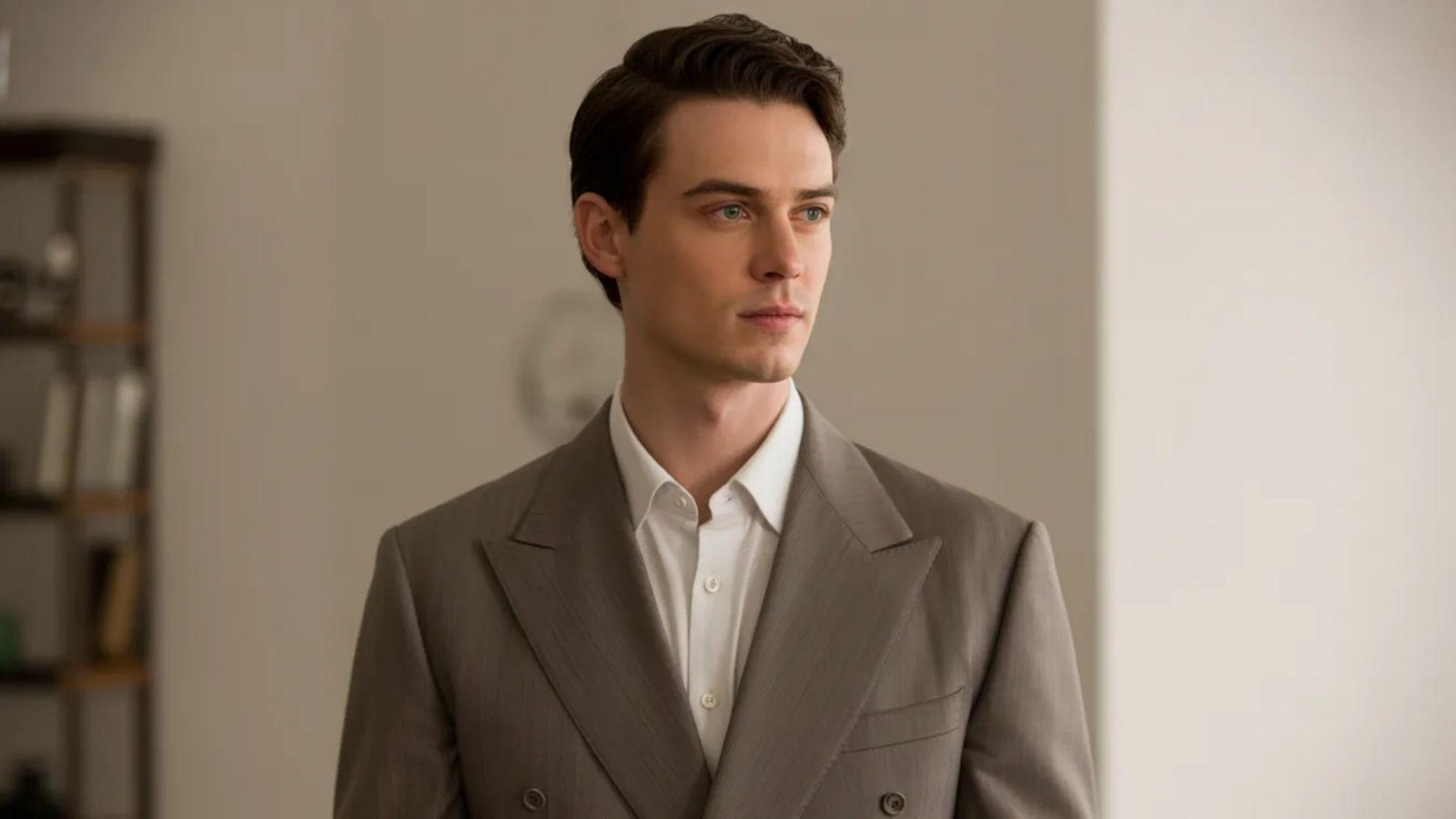 A man dressed in a suit and white shirt poses in a spacious, elegantly decorated room.