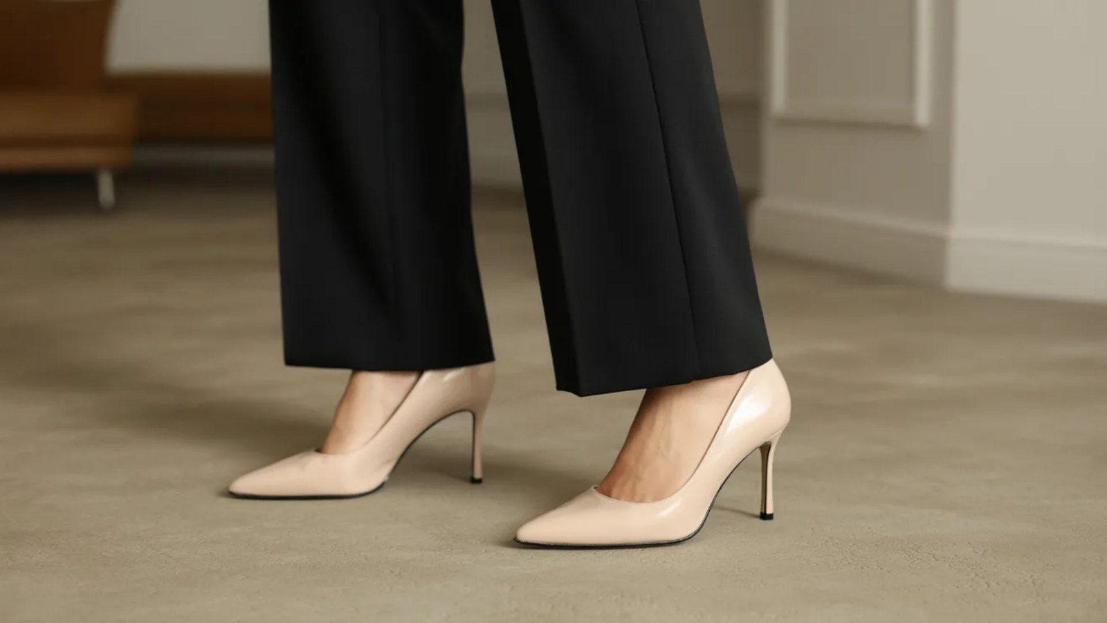 A woman in black pants and nude heels stands confidently, showcasing a stylish and modern outfit.