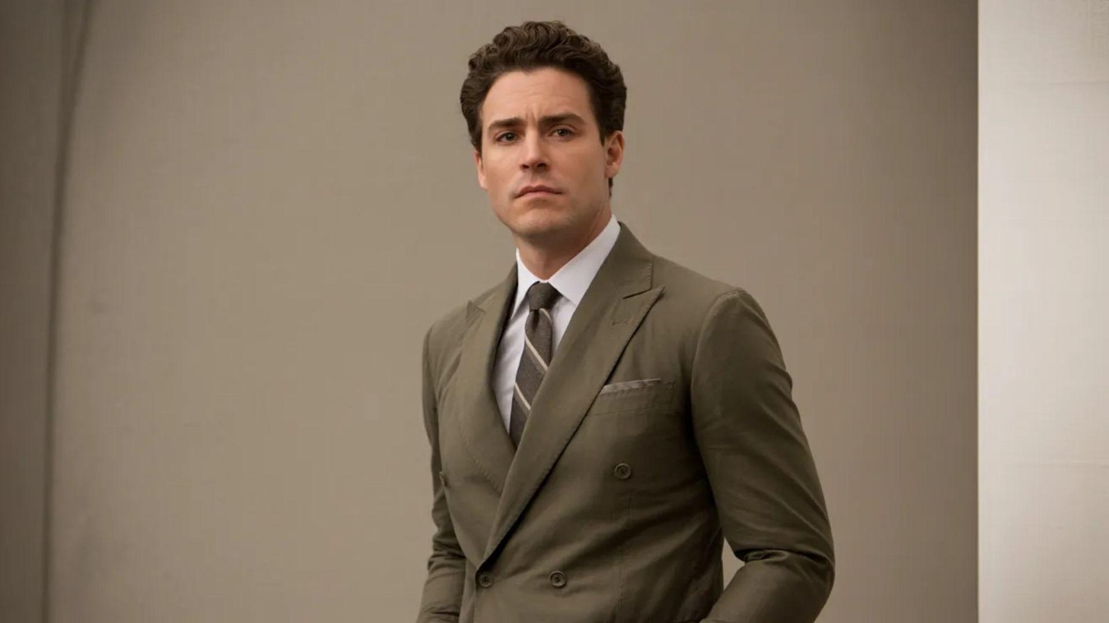  A man in a suit and tie stands confidently in a well-lit room, exuding professionalism and poise.