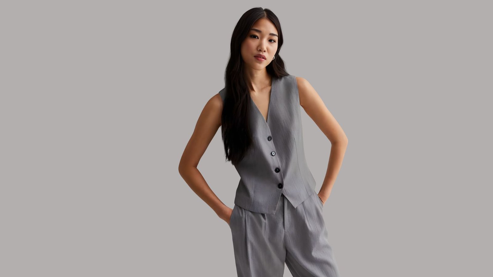 A woman wearing a grey suit and pants stands confidently, showcasing a professional appearance.