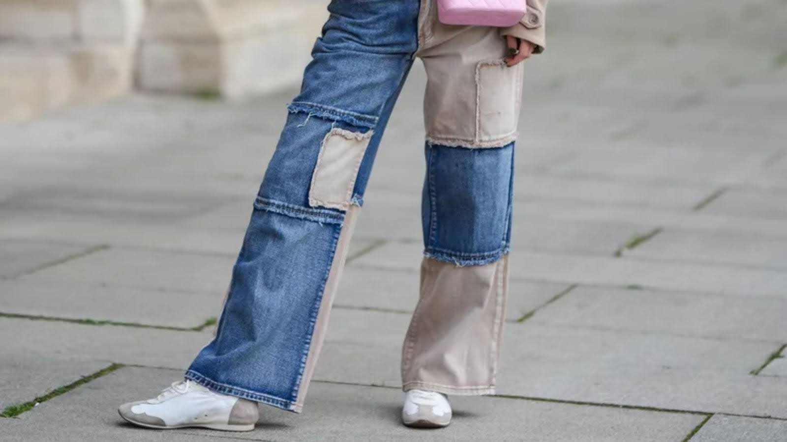 A woman in jeans carries a pink bag, standing confidently against a neutral background.