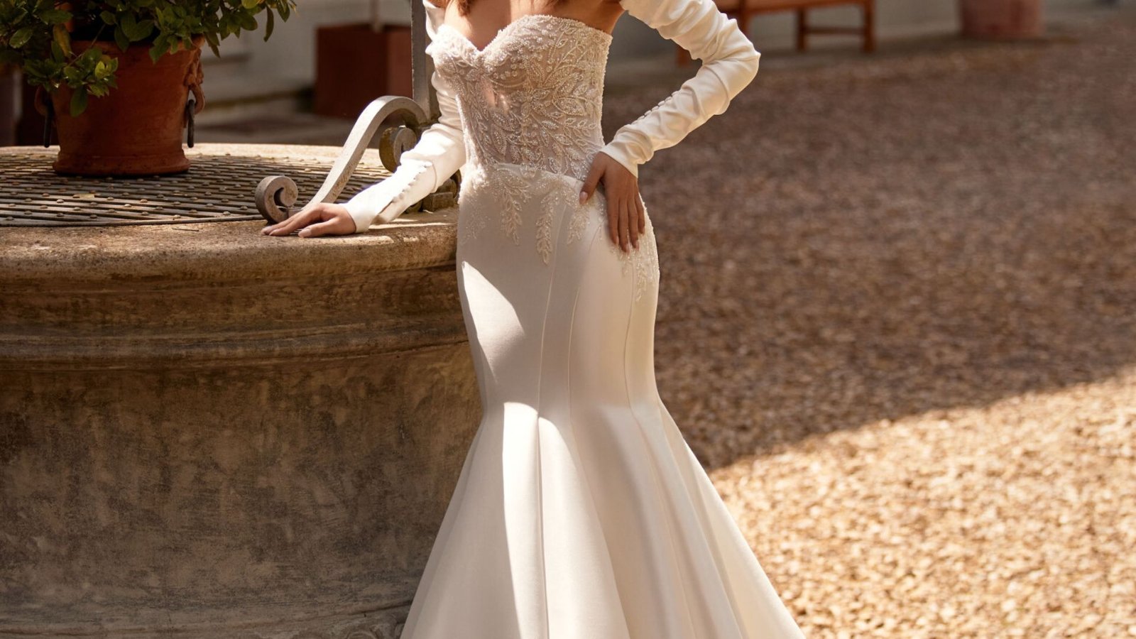 A beautiful woman in a wedding dress leans gracefully against a wall, showcasing elegance and joy on her special day.