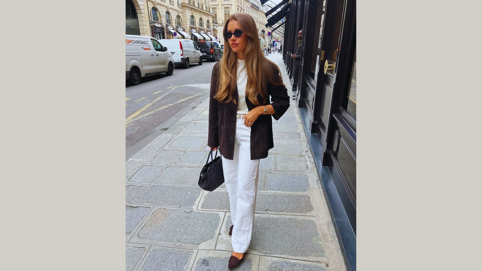 A woman wearing white pants and a black blazer stands confidently, showcasing a professional appearance.