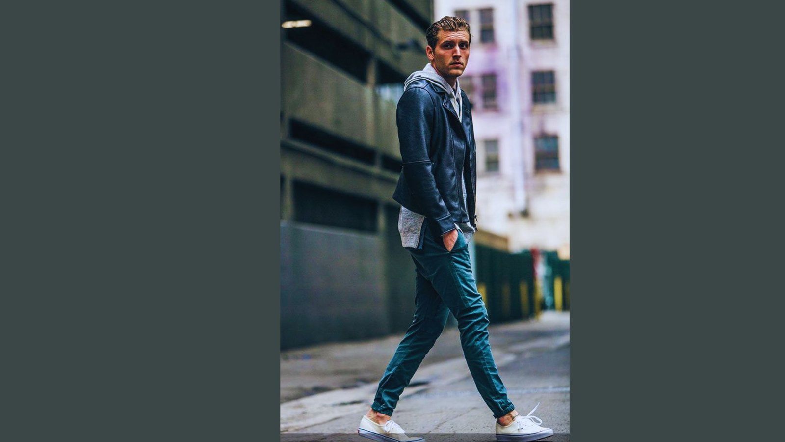 A man wearing jeans and a jacket walks down a city street, surrounded by buildings and pedestrians.
