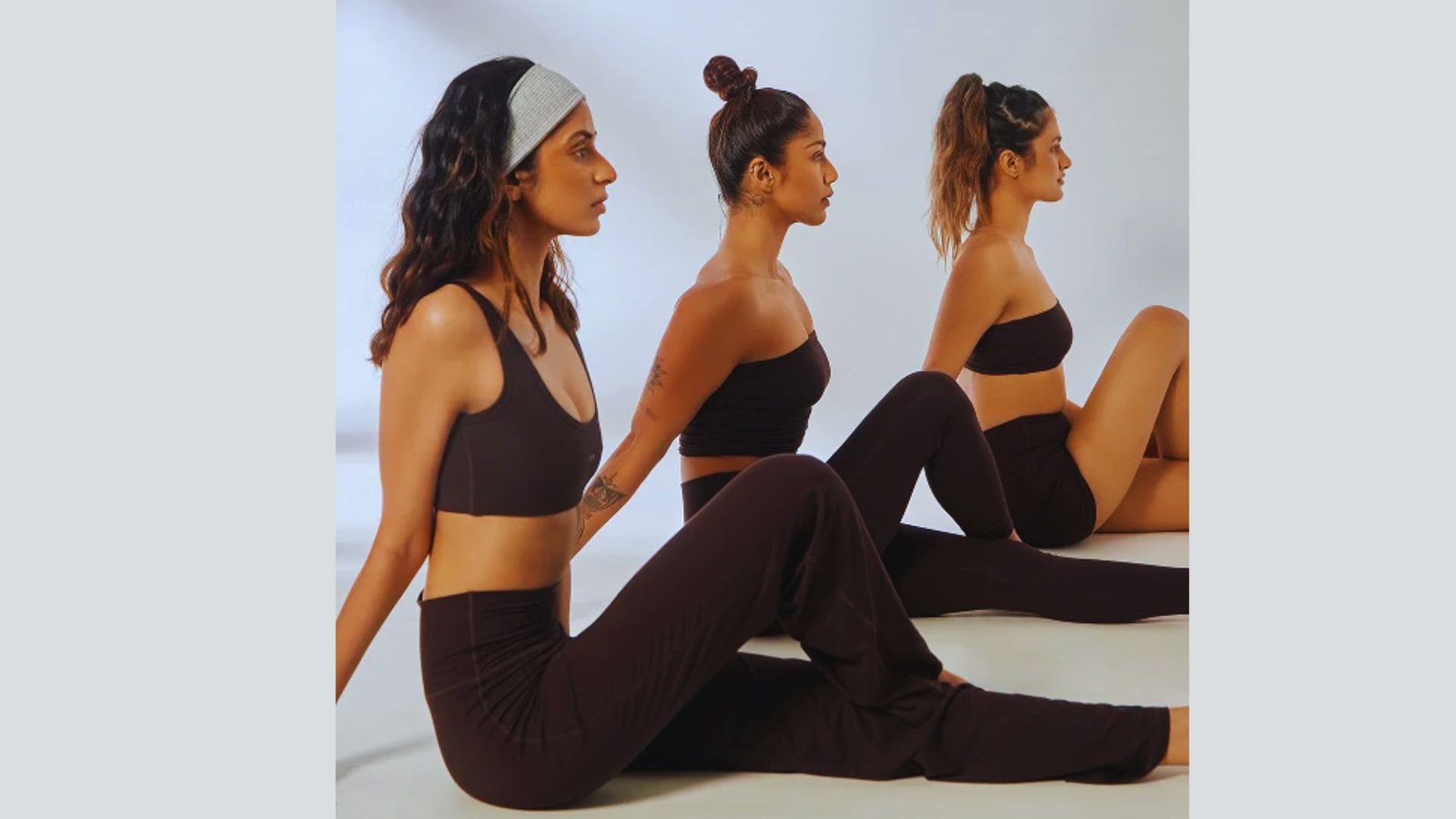 Three women in black yoga pants and headbands sit on the floor, showcasing a classic athleisure yoga fit style.
