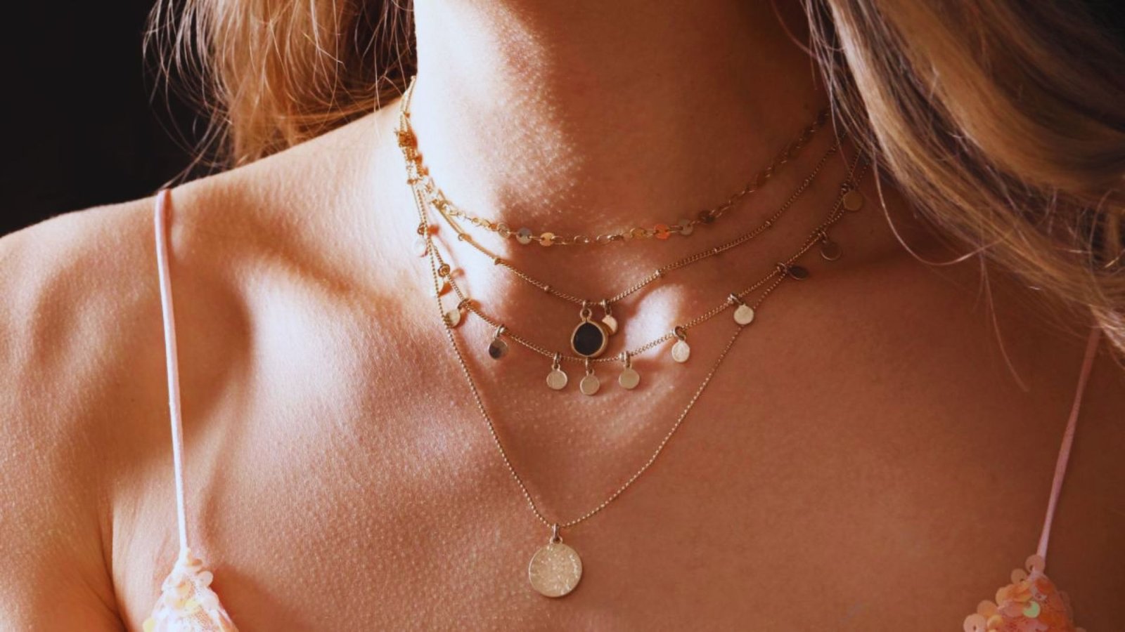 A woman wearing a gold necklace alongside a coin necklace, showcasing her elegant jewelry choices.