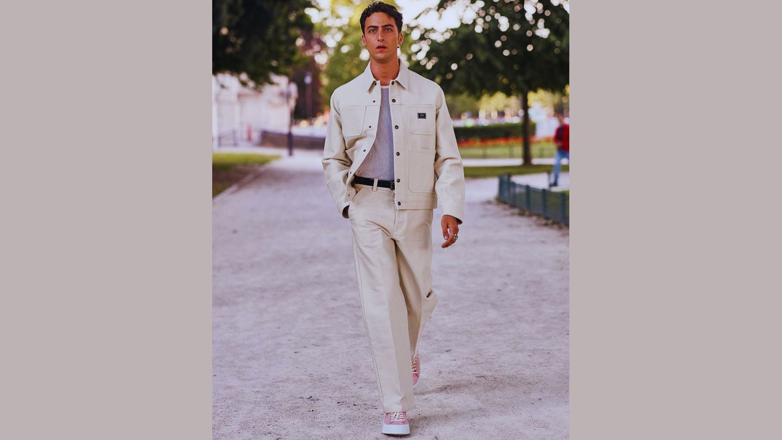  A man dressed in a white suit and shoes strolls along a sidewalk, exemplifying modern formal streetwear fashion.
