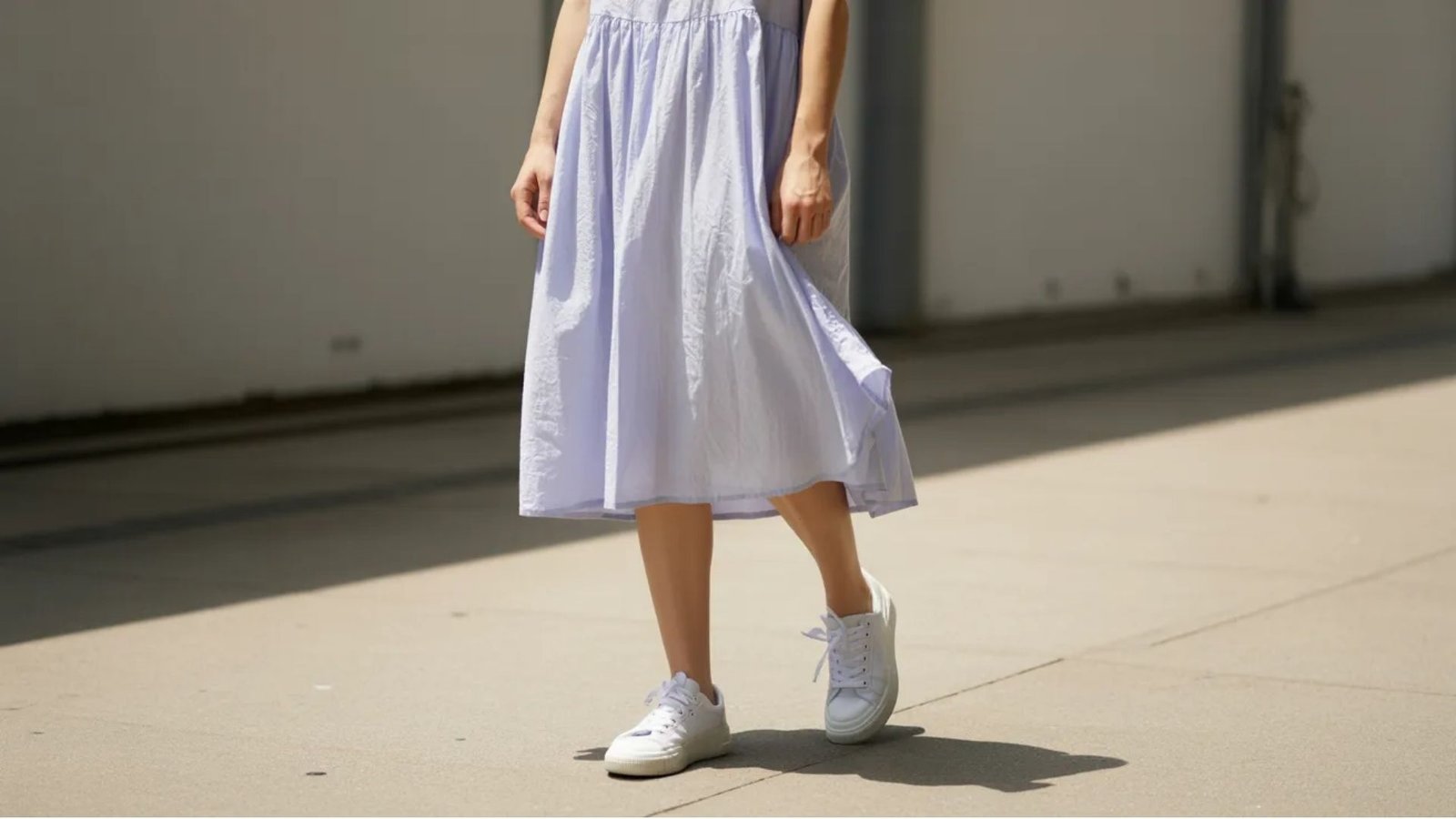 A woman wearing a blue dress and white sneakers stands confidently, showcasing a casual yet stylish outfit.
