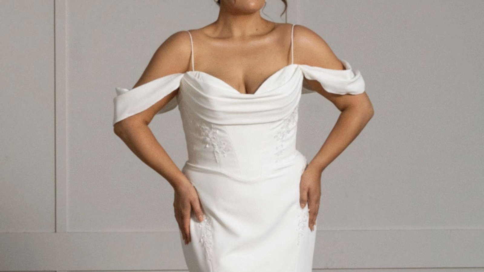 A woman in a white wedding dress poses elegantly for a photo, showcasing her joyful expression and beautiful attire.