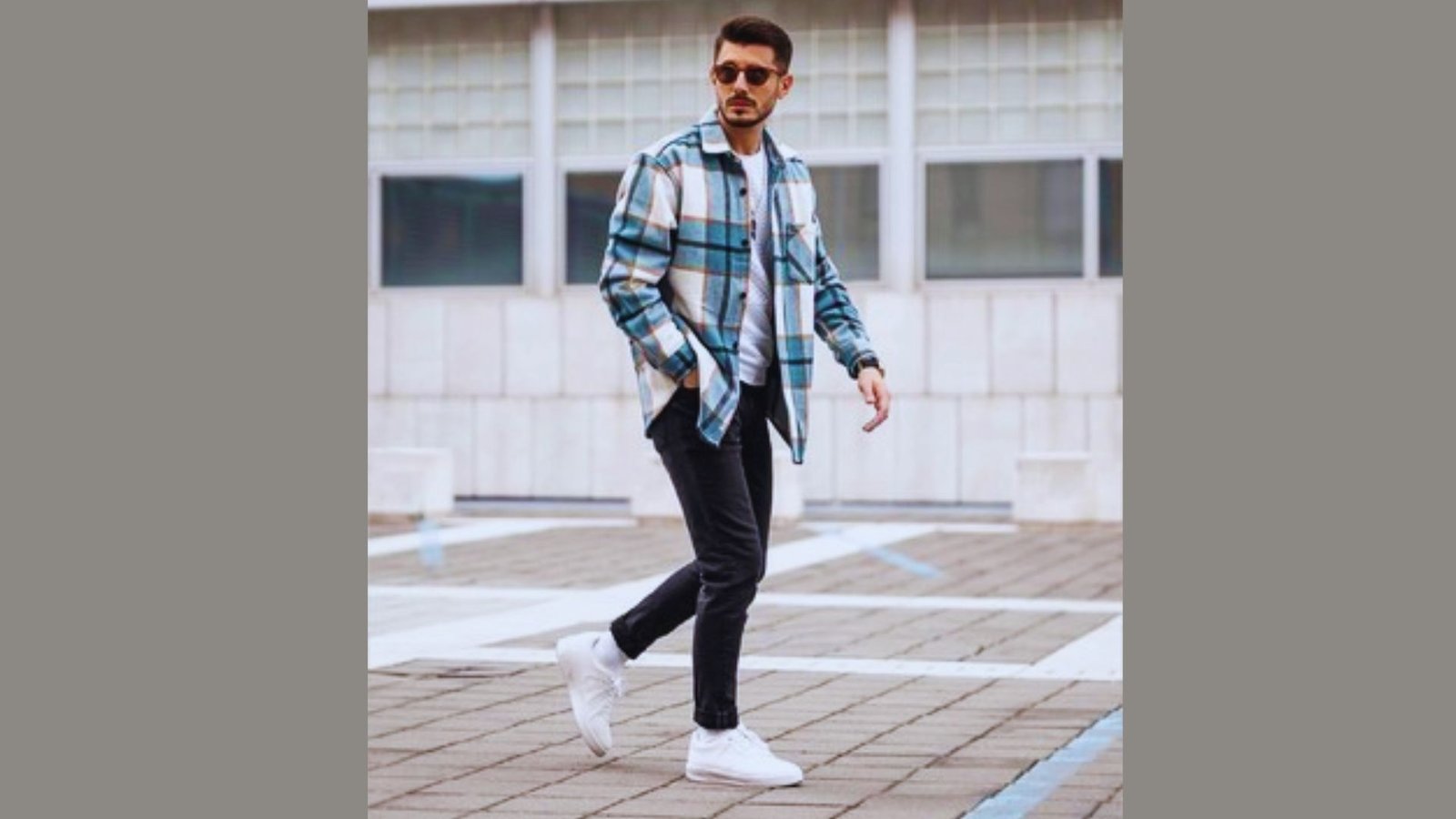  A man wearing a plaid shirt and jeans walks along a city street, surrounded by buildings and parked cars.