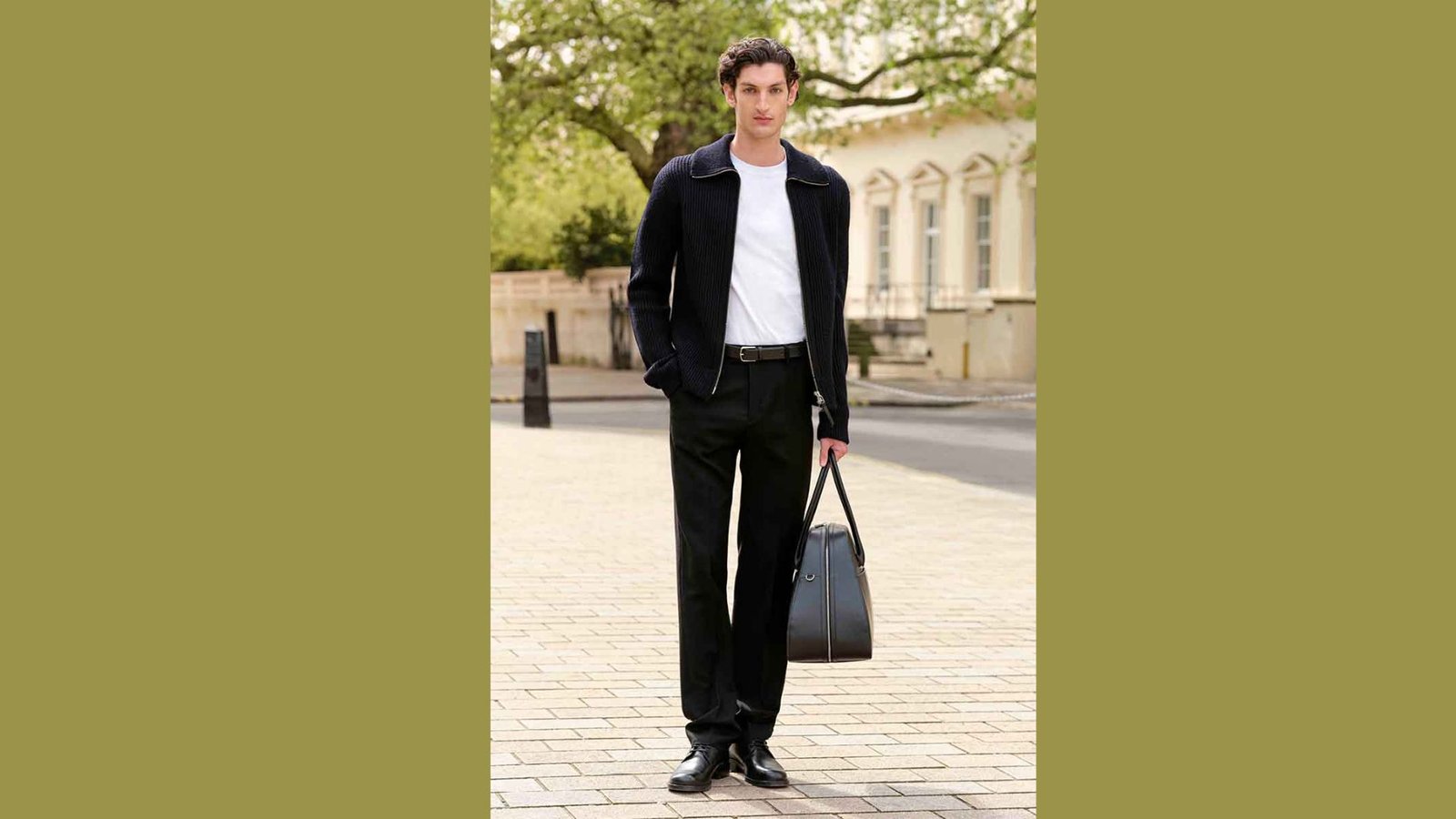 A man wearing a suit and tie stands on a brick sidewalk, presenting a polished and formal demeanor.