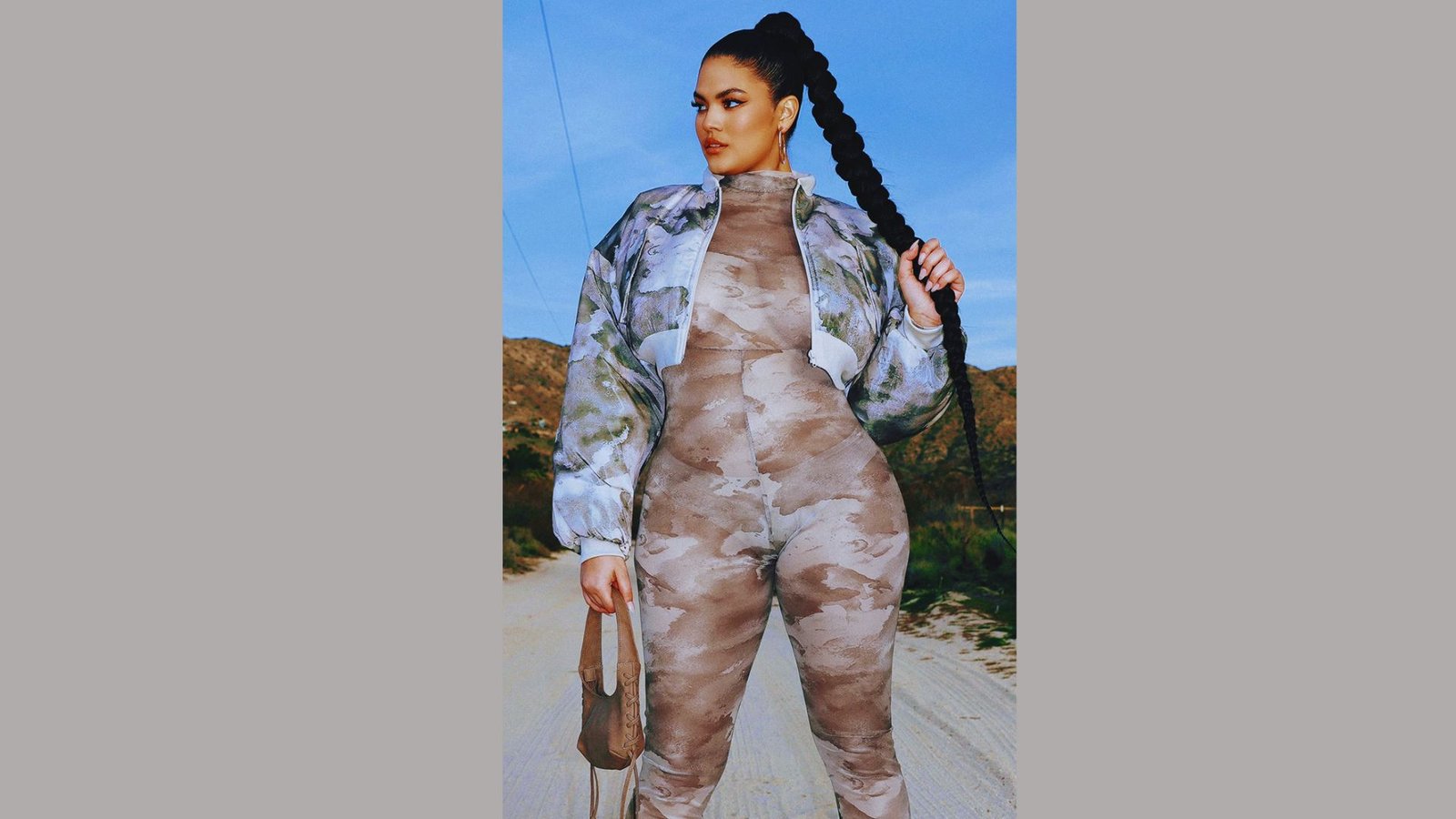 A woman in a camouflage jumpsuit and cropped puffer jacket stands confidently on a road.

