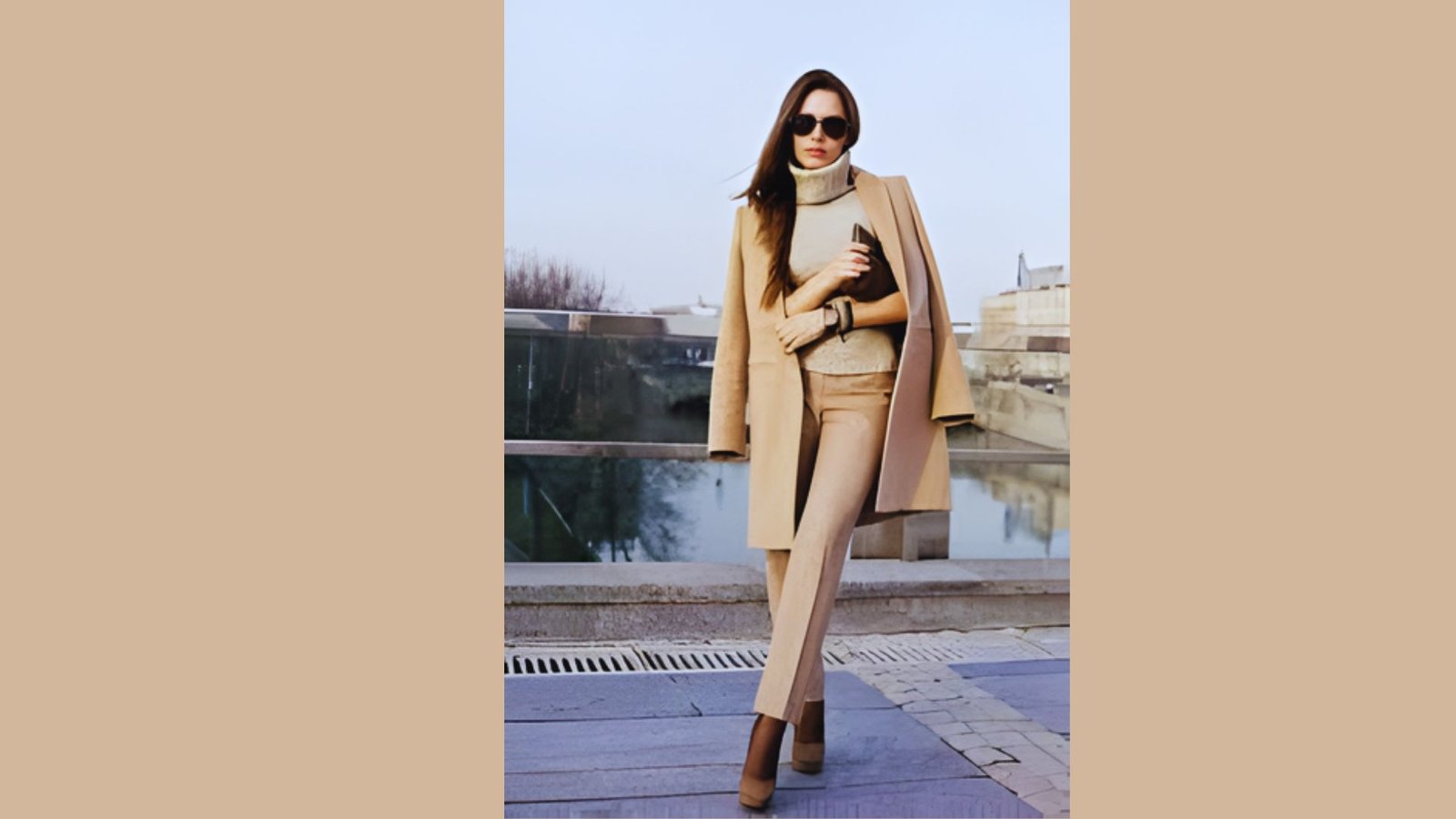A woman wearing a tan coat and sunglasses stands confidently, showcasing her stylish outdoor attire.