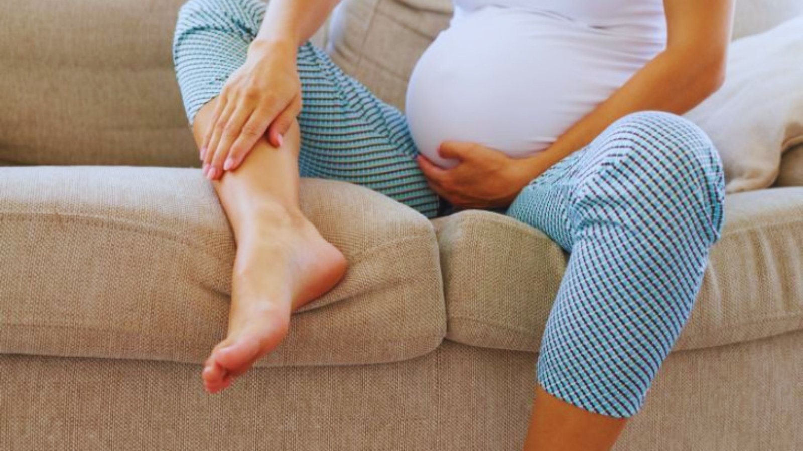 A pregnant woman seated on a couch ,representing foot discomfort in the third trimester.