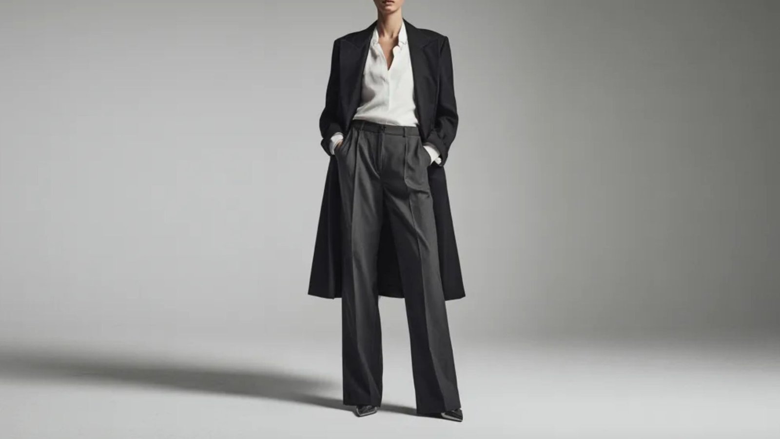 A woman dressed in a black coat and pants poses elegantly, highlighting her fashionable attire.