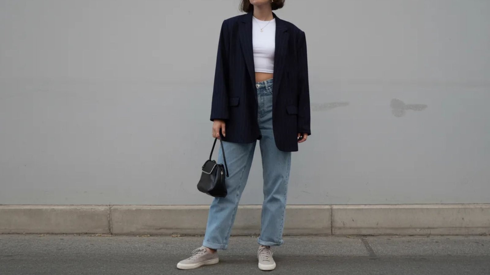 A woman in a crop top and jeans stands confidently, showcasing a casual and stylish outfit.