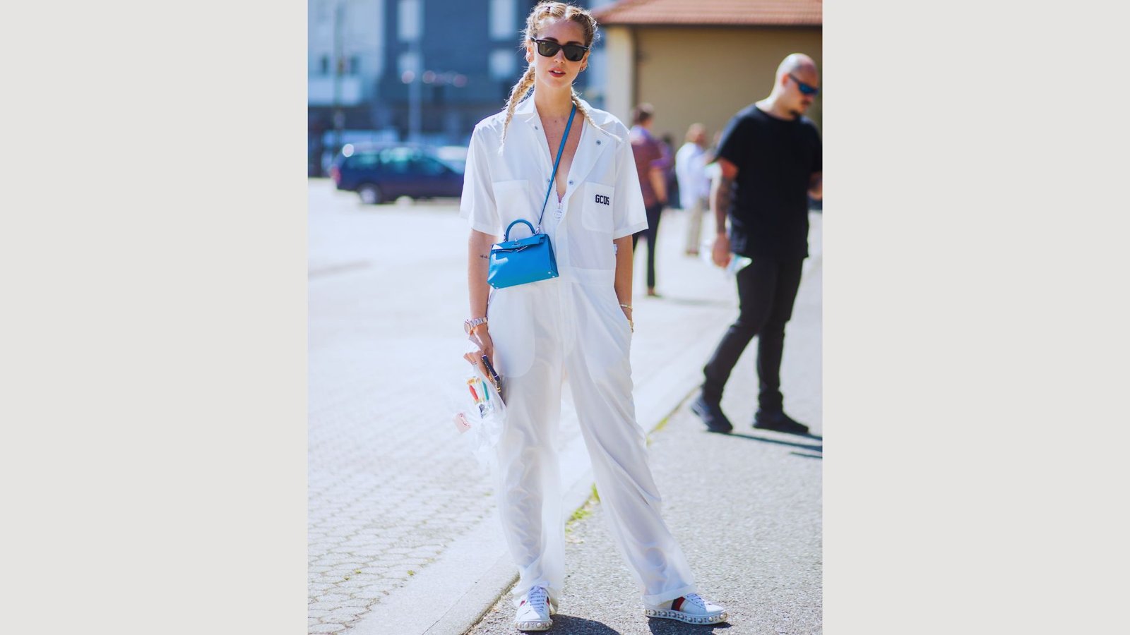 A woman wearing a white jumpsuit and sunglasses stands confidently, showcasing a stylish summer look.

