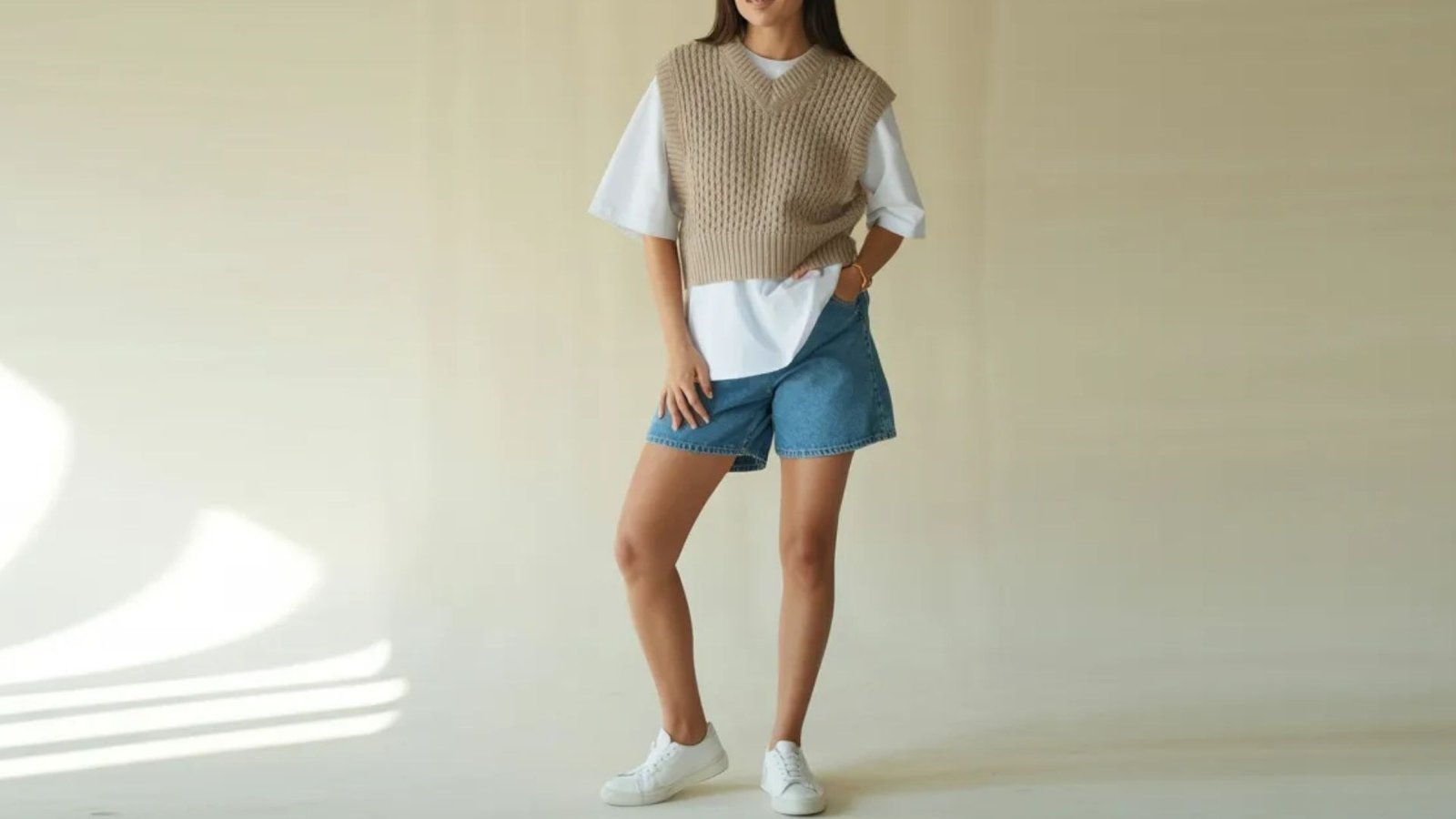 A woman in a white shirt and denim shorts smiles while standing in a vibrant outdoor environment.