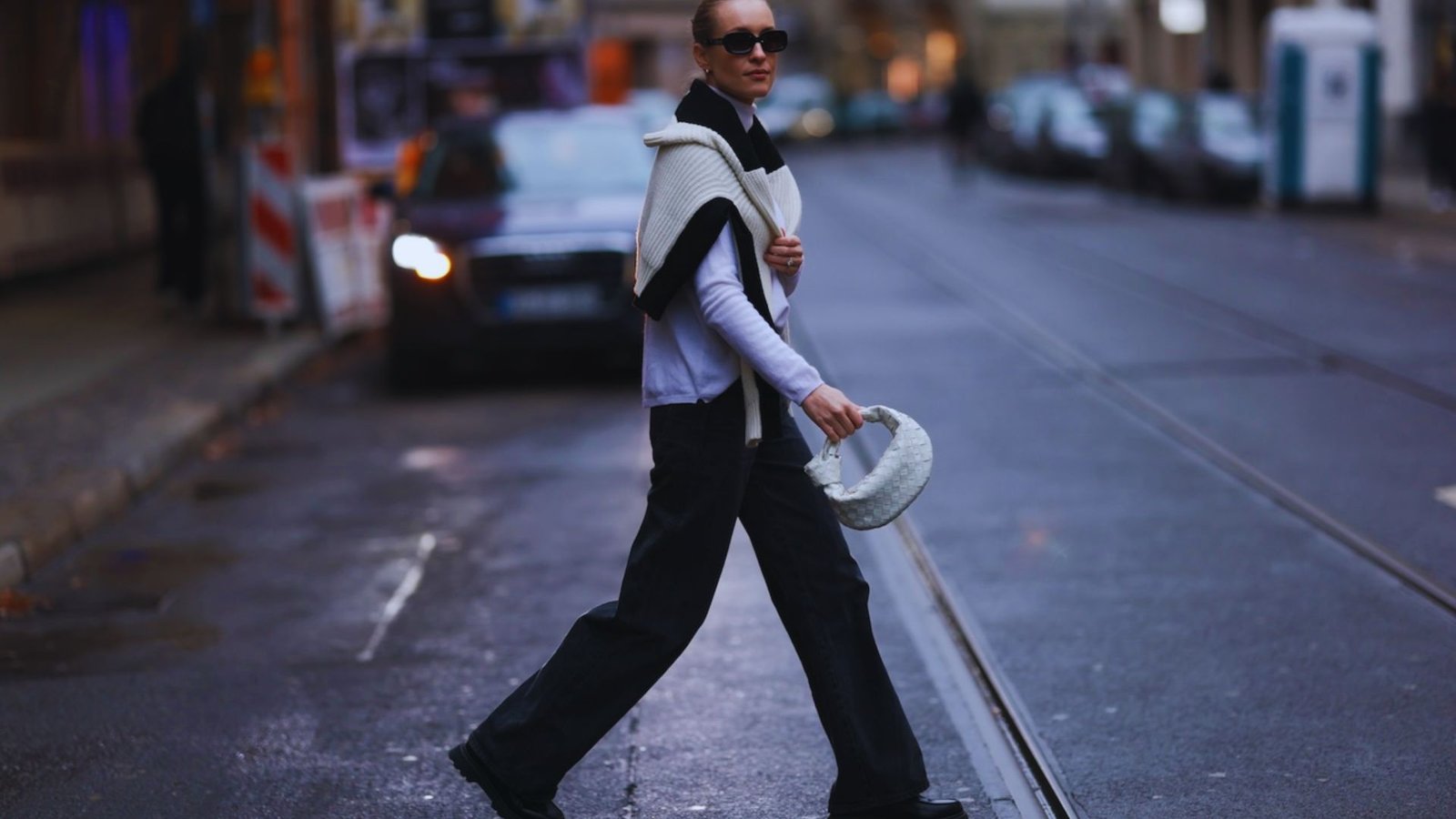A woman walks down a street, wearing a stylish hat and sunglasses, enjoying a sunny day.