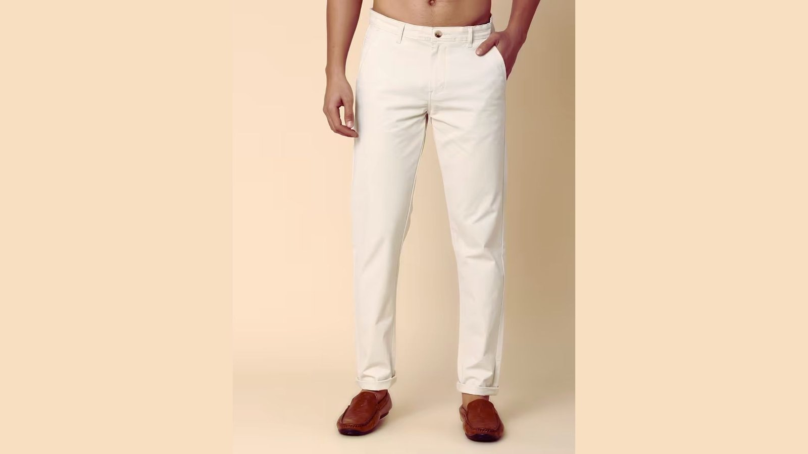 A man stands confidently, dressed in a white shirt and white pants, against a neutral background.