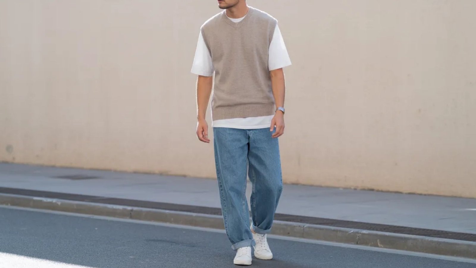 A man wearing a beige vest and jeans walks down the street, surrounded by urban scenery.