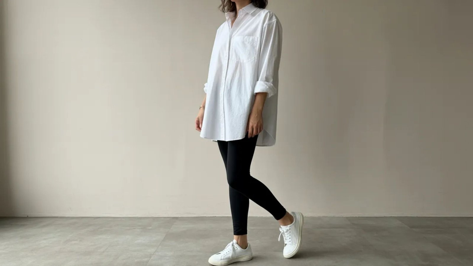 A woman in a white shirt and black leggings stands confidently, showcasing a casual yet stylish outfit.