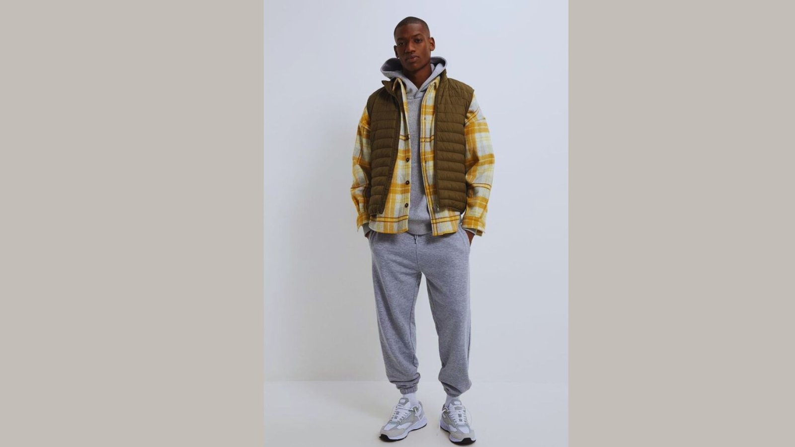 A man wearing a yellow plaid shirt and grey sweatpants stands casually, showcasing a relaxed outfit.