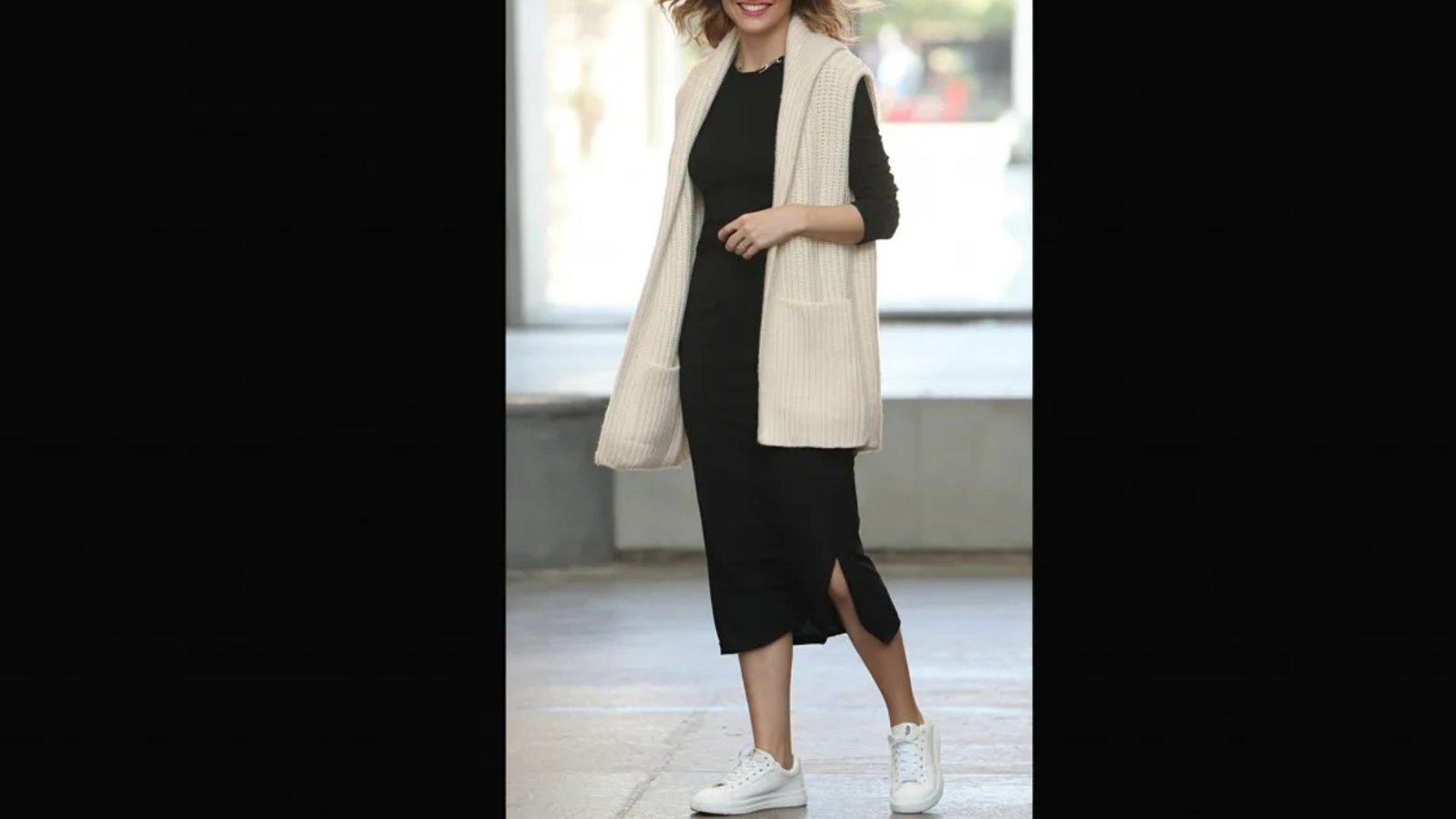 A woman in a sleek black dress paired with white shoes poses elegantly, highlighting her fashion choice.