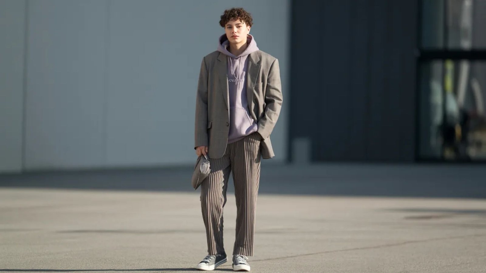 A man wearing a grey suit over a purple sweater, standing confidently with a neutral expression.