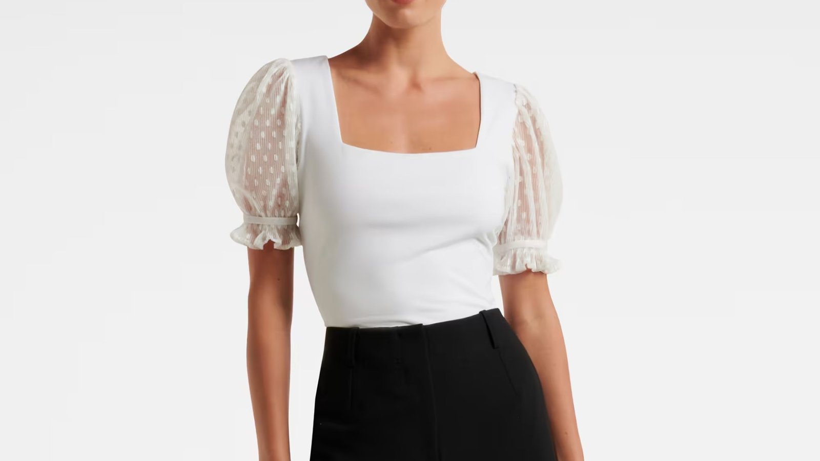 A model is dressed in a white top paired with black pants, showcasing a simple yet stylish outfit.