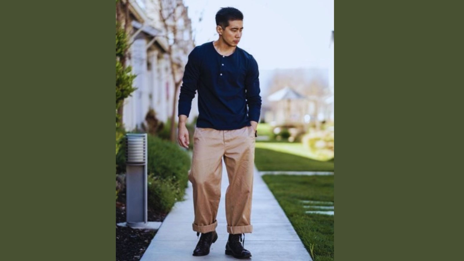 A man in a blue shirt and tan pants walks along a sidewalk, surrounded by greenery and urban scenery.