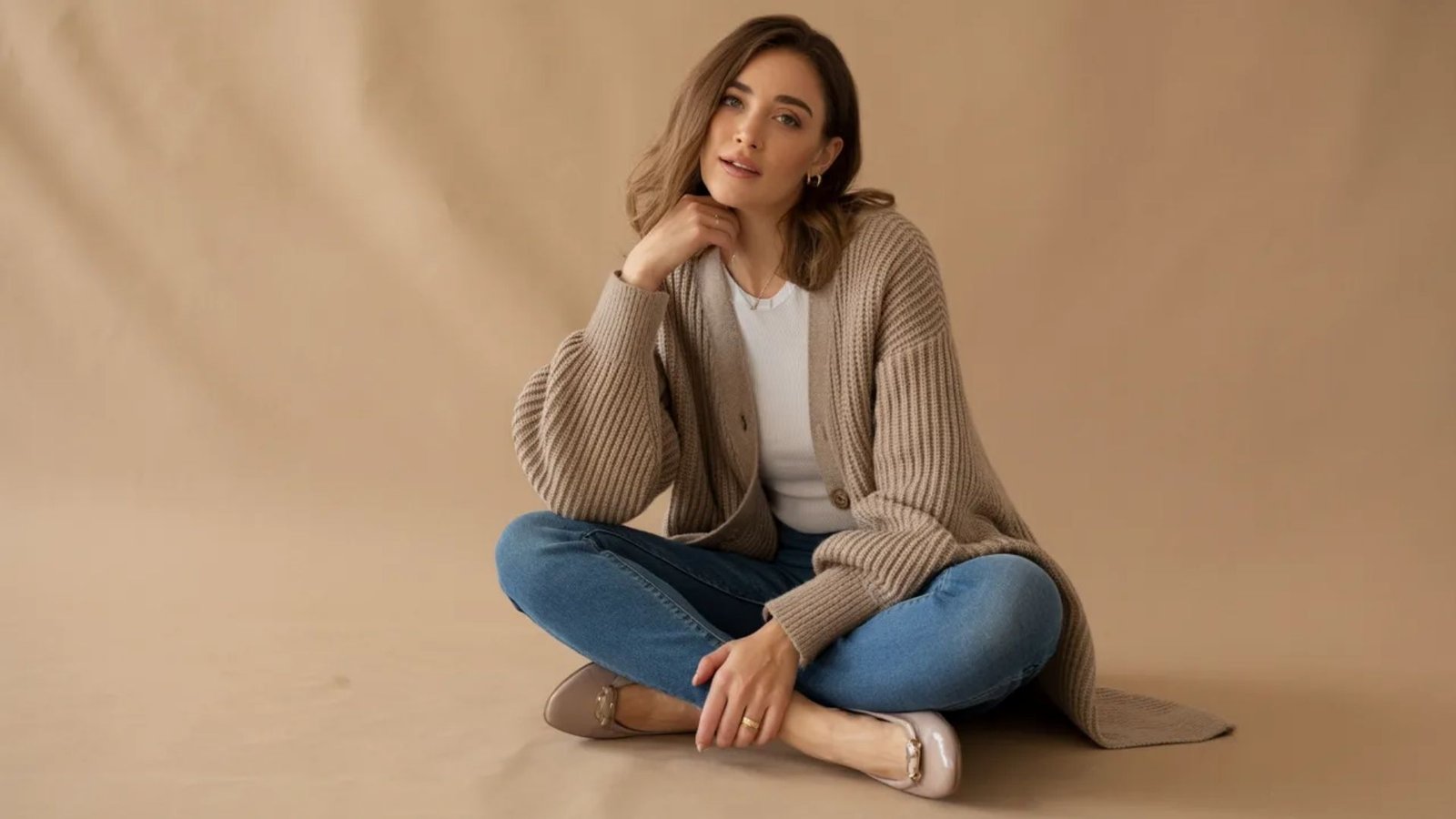 A woman in a sweater and jeans sits on the floor, looking relaxed and comfortable.