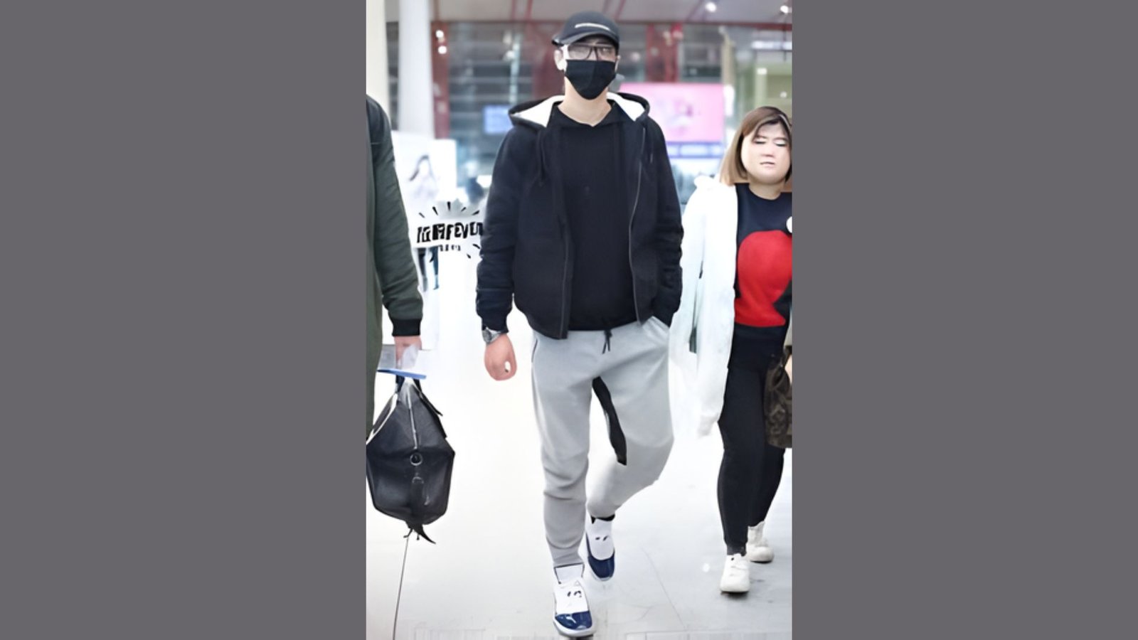 A man in a mask and black shirt walking through an airport terminal.