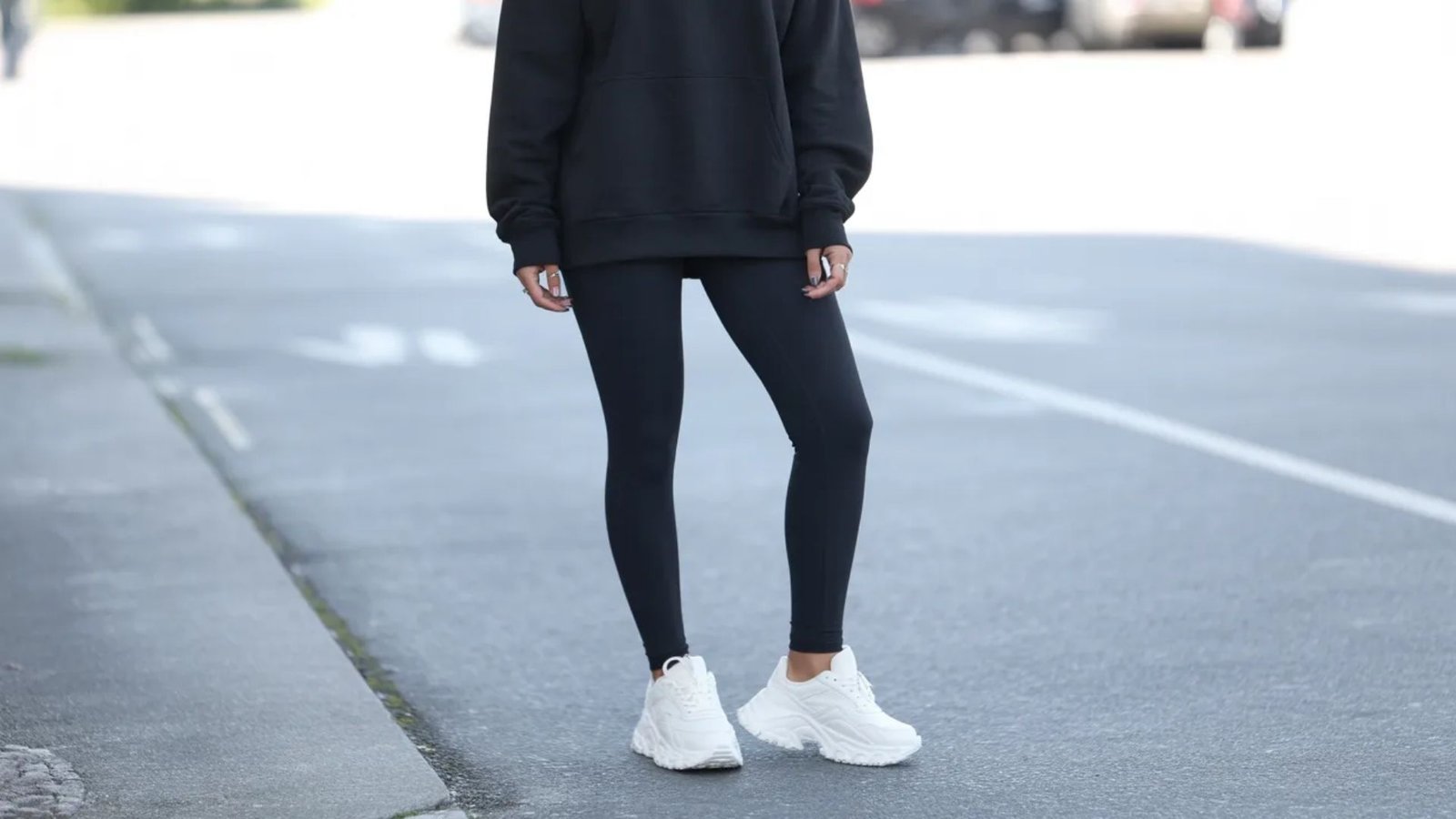 A woman wearing a black sweatshirt and leggings stands confidently on the street.
