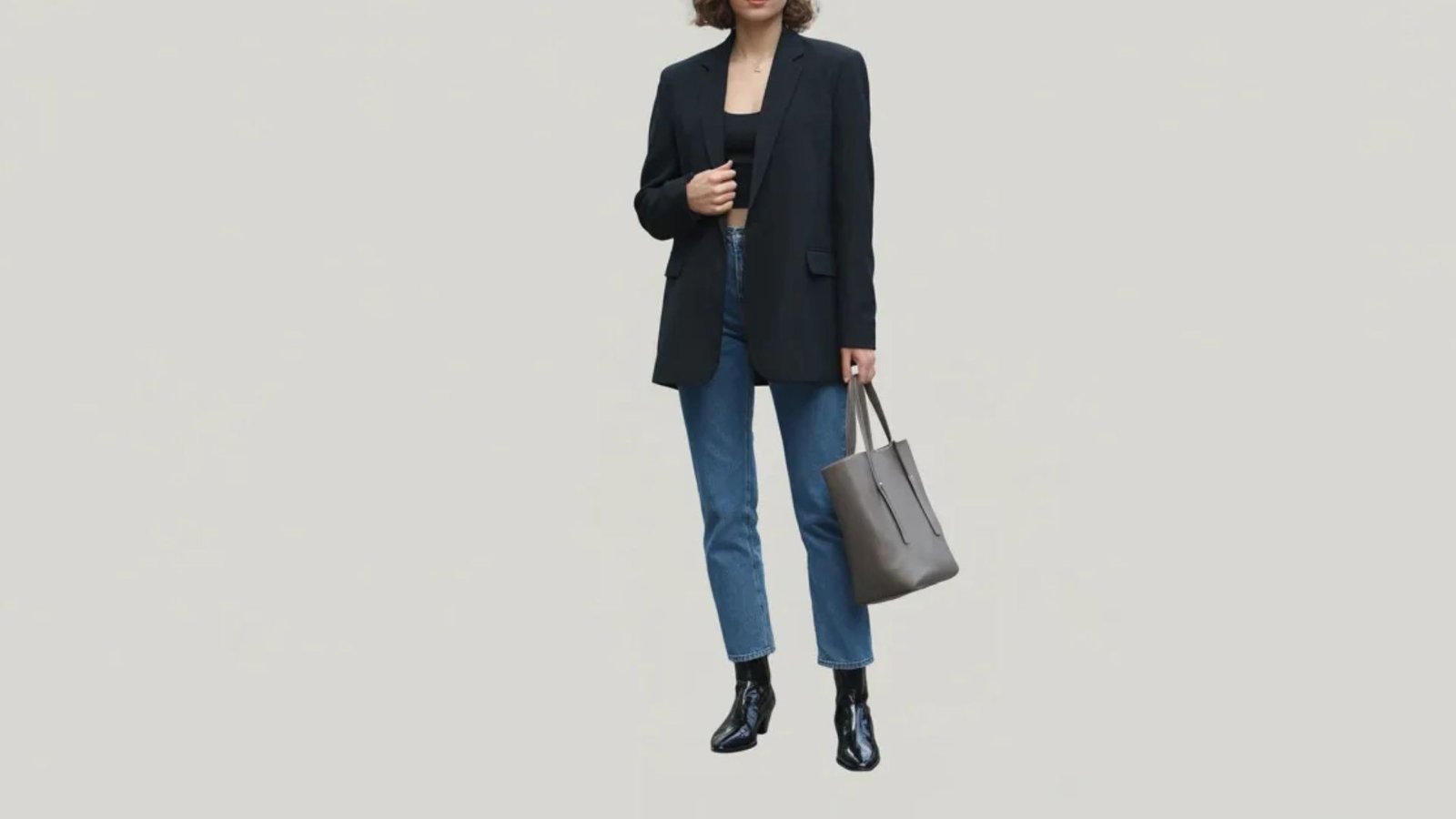 A woman wearing jeans and a blazer stands confidently, showcasing a professional yet casual style.