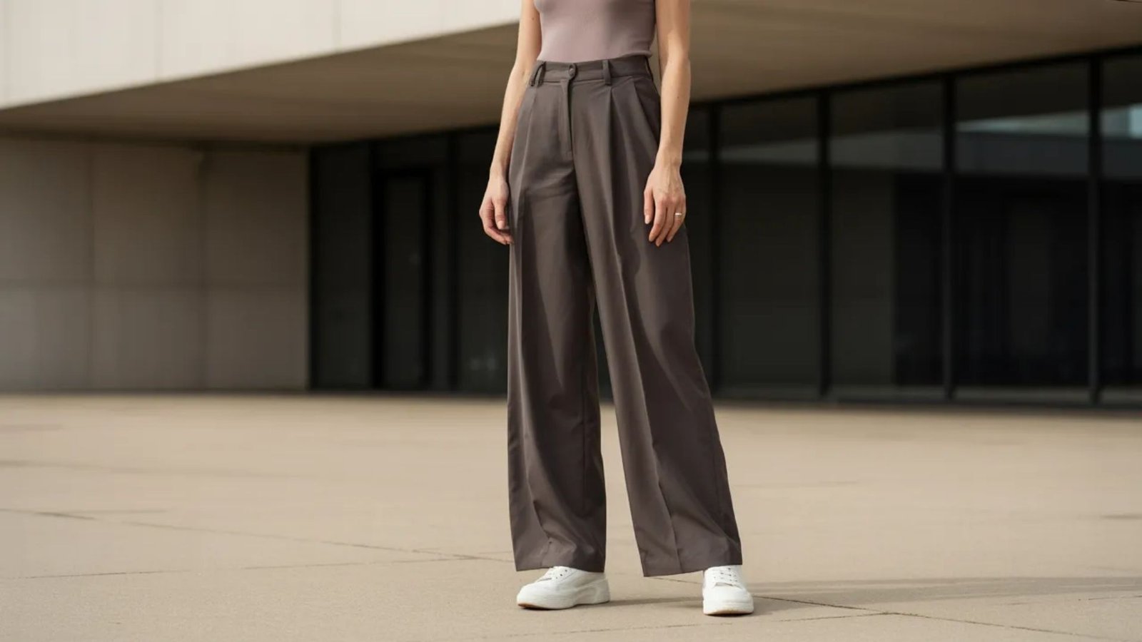 A woman in a grey top and wide pants stands confidently, showcasing a relaxed and stylish outfit.