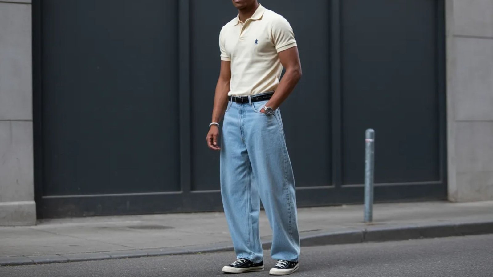 A man in a polo shirt and blue jeans stands, embodying a laid-back and contemporary style.