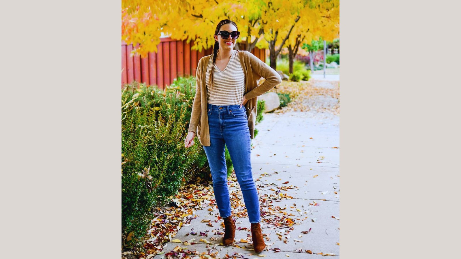A woman wearing jeans and a sweater stands on a sidewalk, looking confidently ahead.