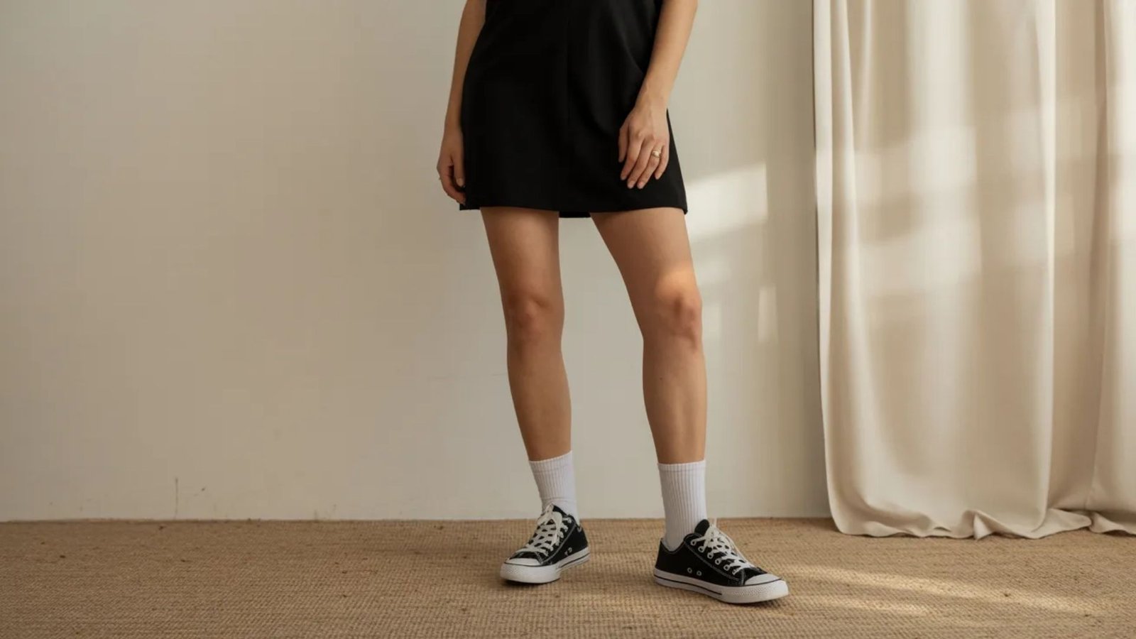 A woman wearing a black dress paired with sneakers stands confidently, showcasing a blend of elegance and casual style.