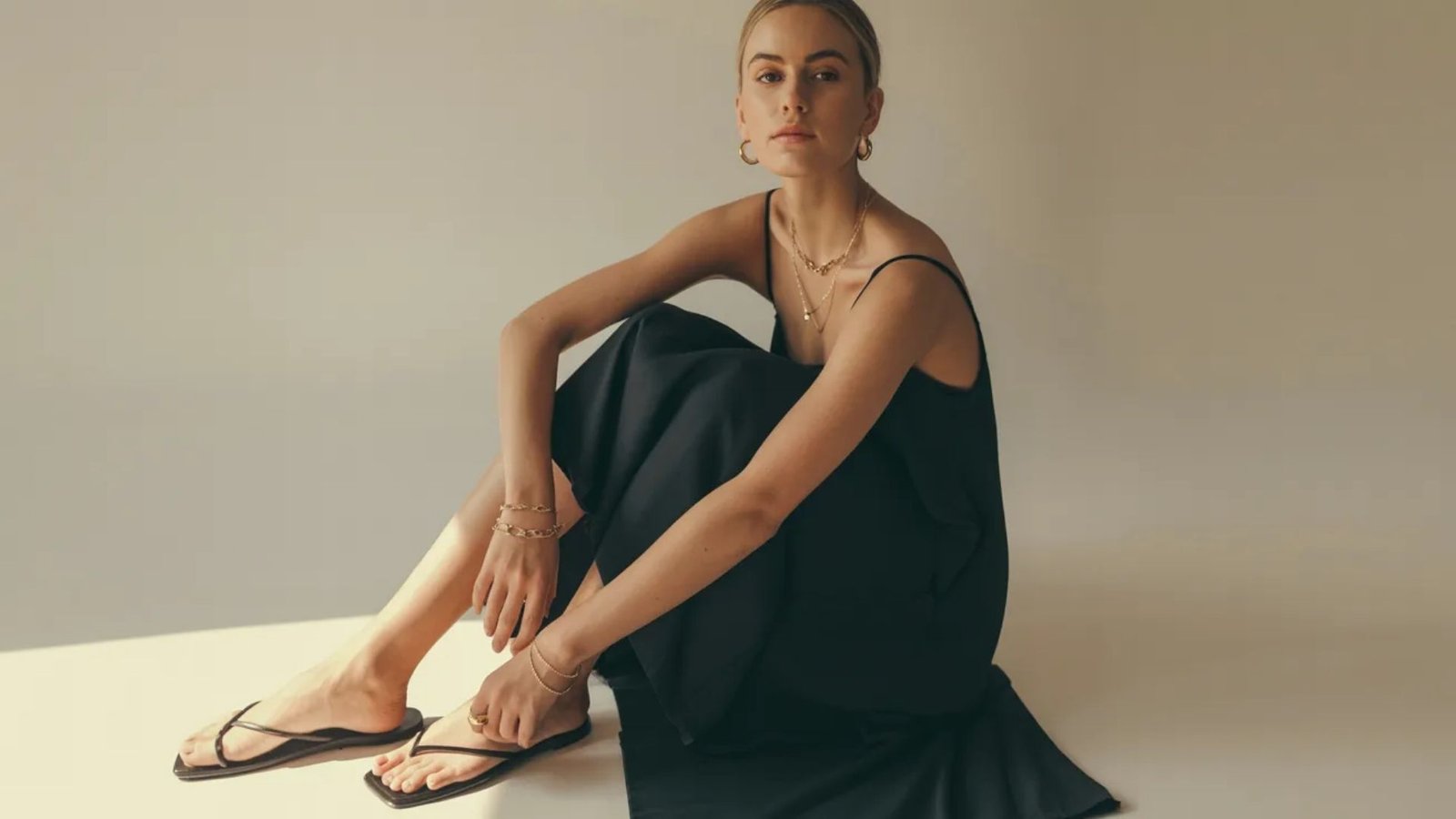 A woman in a black dress sits on the floor, appearing thoughtful and at ease in her surroundings.